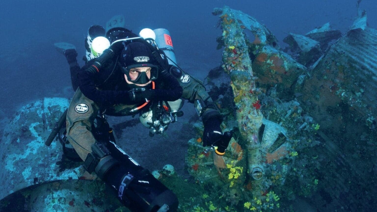 Technical diver in twin-tank configuration over a colourful deep wreck