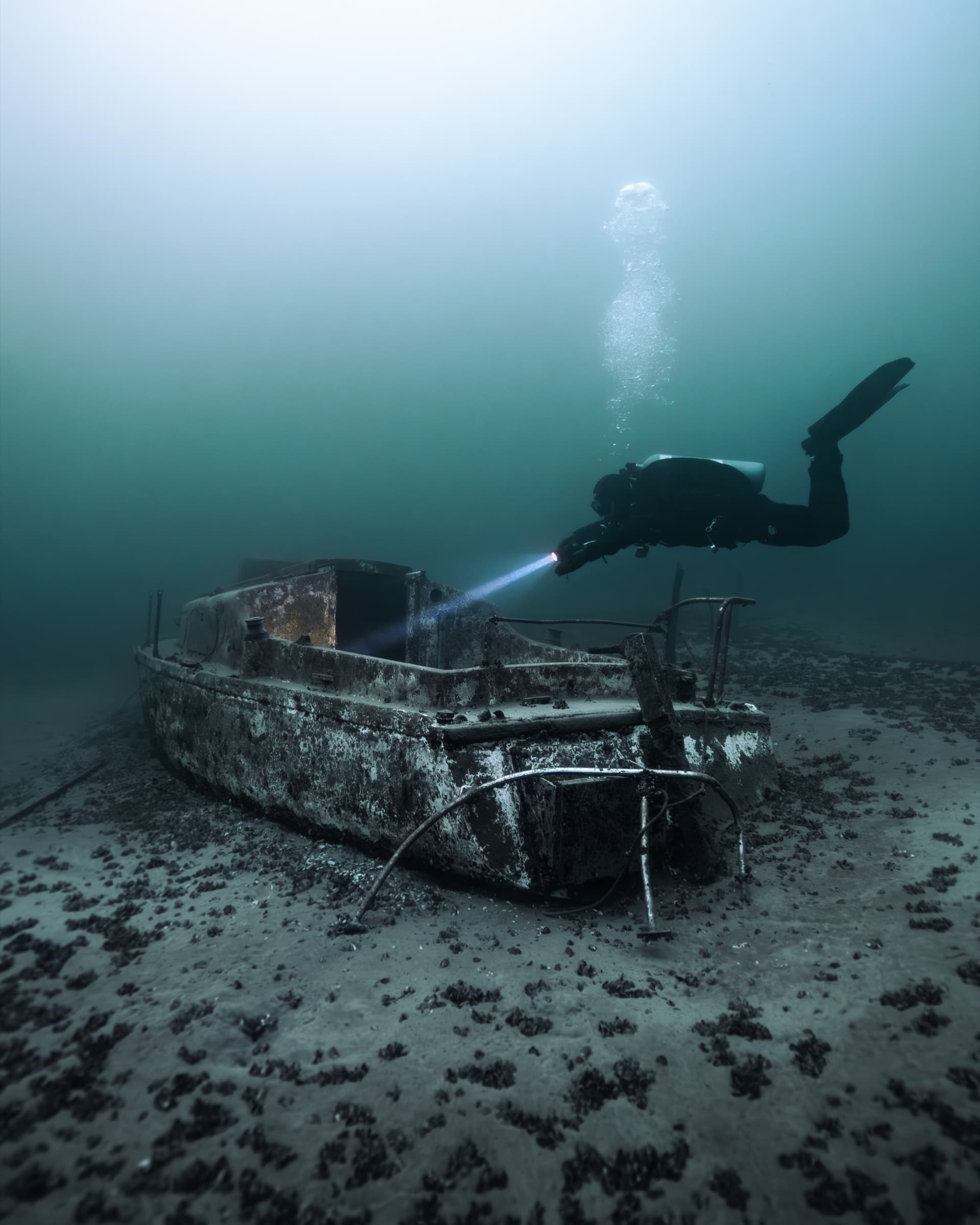 Technical diver illuminating a wreck on the seabed with a torch beam